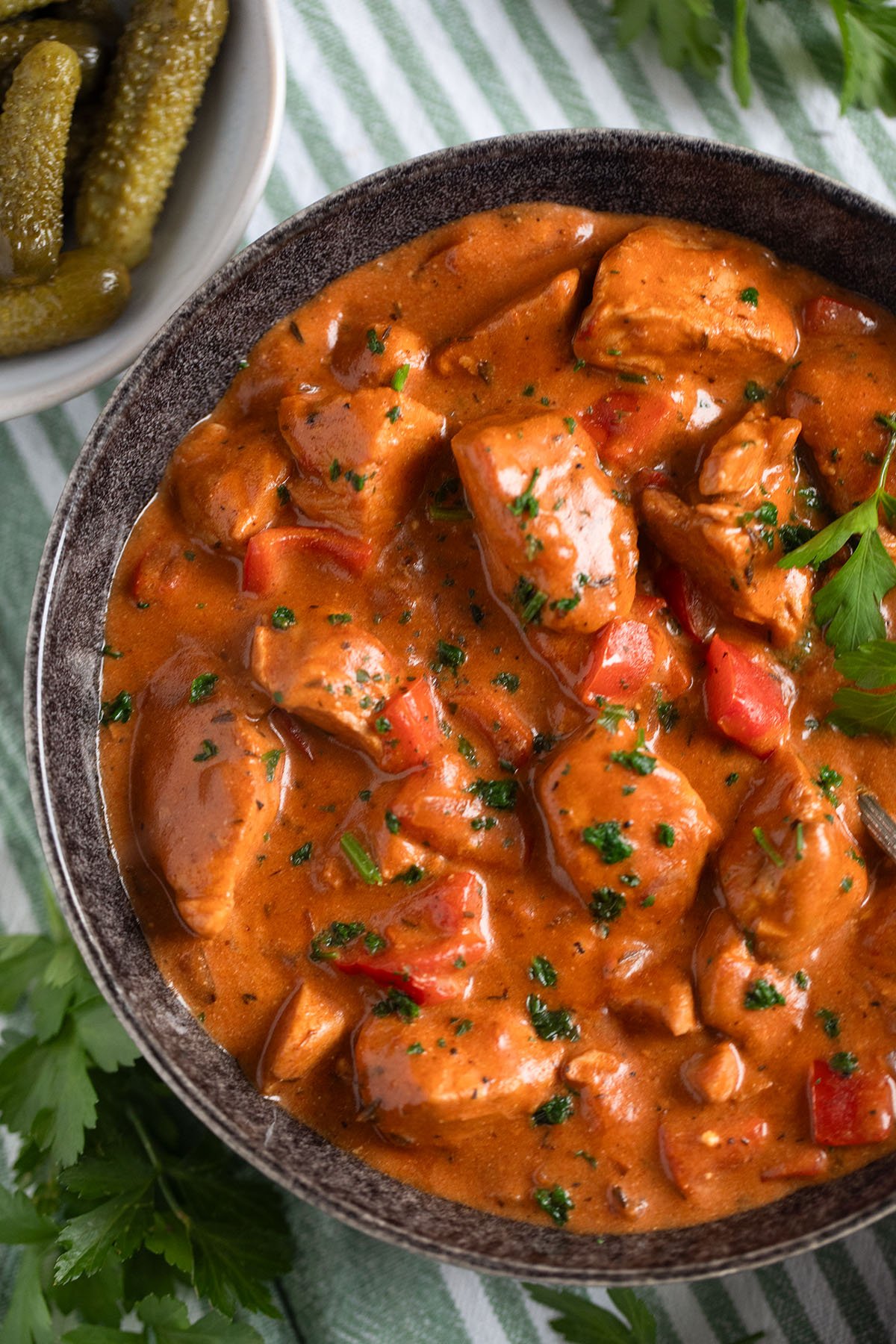 super creamy turkey paprikash with peppers in a bowl, a small bowl of gherkins near it.