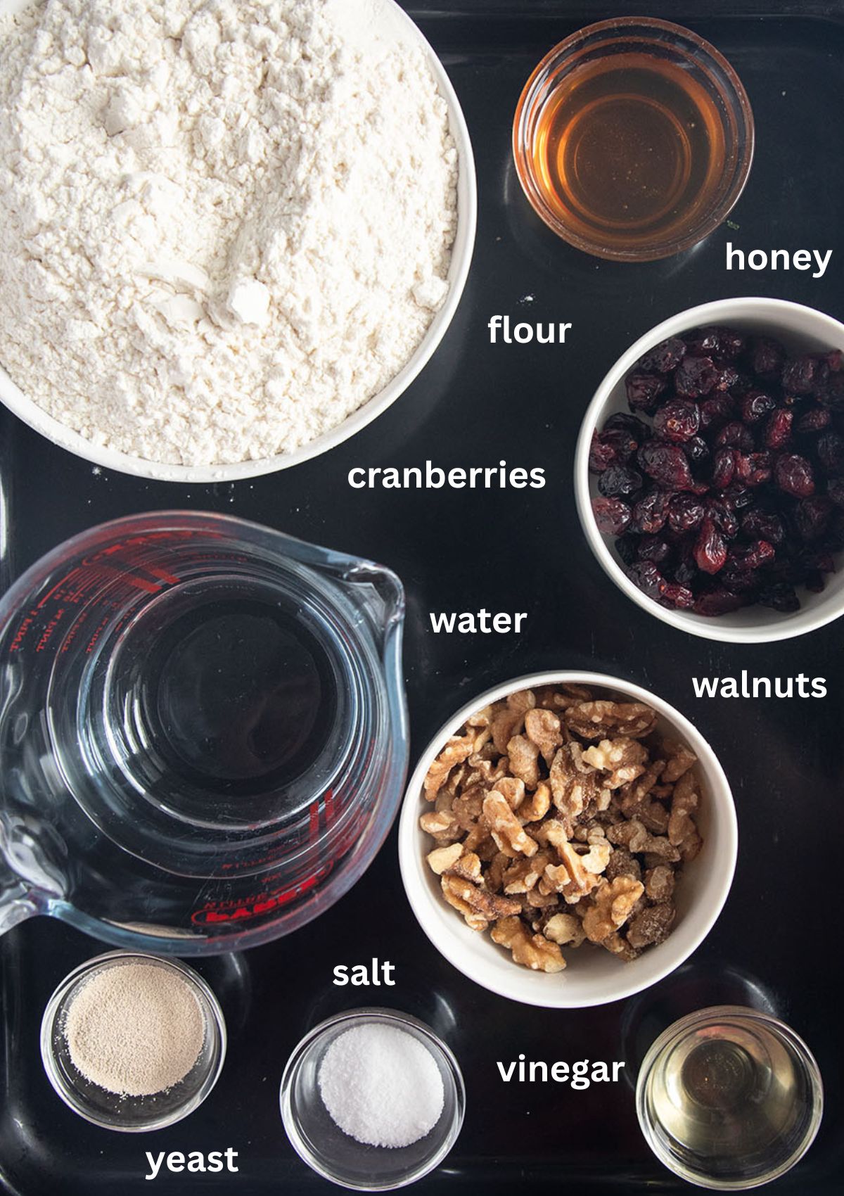 labeled ingredients for making bread with flour, honey, walnuts, cranberries, yeast, salt and vinegar.
