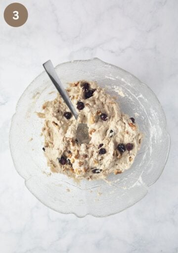 adding cranberries and walnuts to bread dough in a bowl.