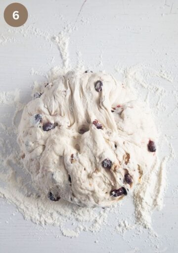 a ball of dough on the floured table to make bread with walnuts and cranberries.