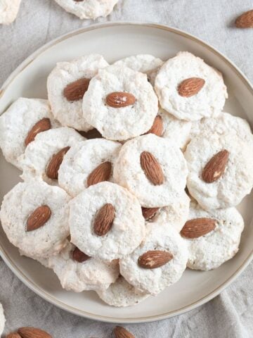 a plate full of almond macaroons and many more around the plate.