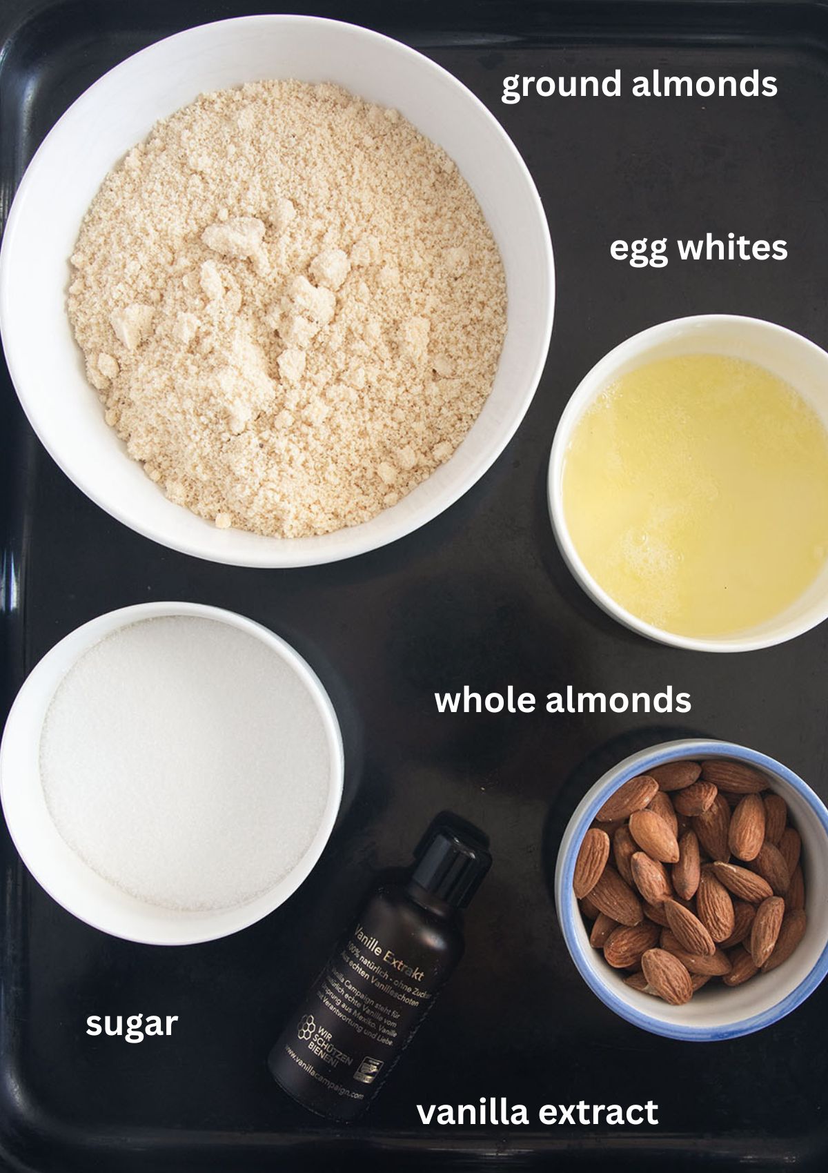 bowls with ground almonds, egg whites, sugar, whole almonds and a bottle of vanilla extract to make macaroons.