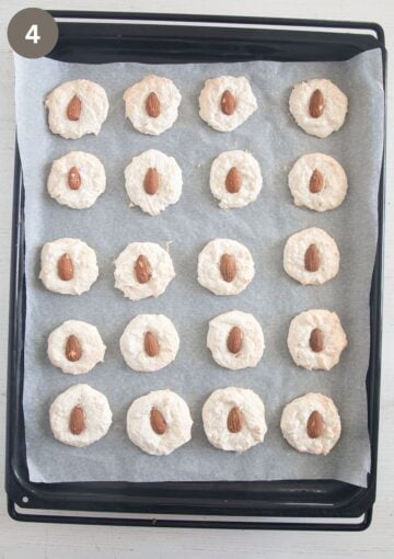 freshly baked macaroons with a whole almond in the middle on a baking sheet lined with parchment paper.