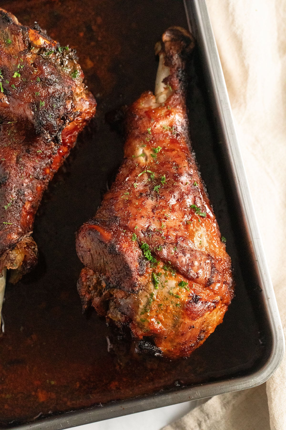baked turkey drumsticks resting in a roasting pan and sprinkled with parsley.