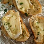 brie baguette sprinkled with parsley on a piece of aluminum foil.