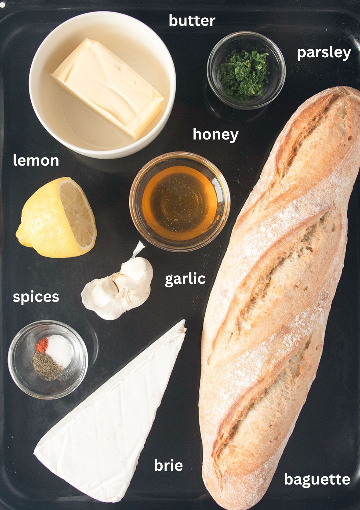 labeled ingredients for making baguette stuffed with brie, butter, honey, garlic and parsley.