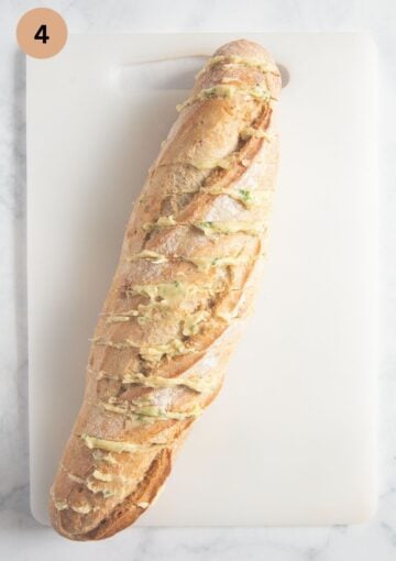 bagutte stuffed with garlic and herb butter on a cutting board before stuffing with cheese and baking.