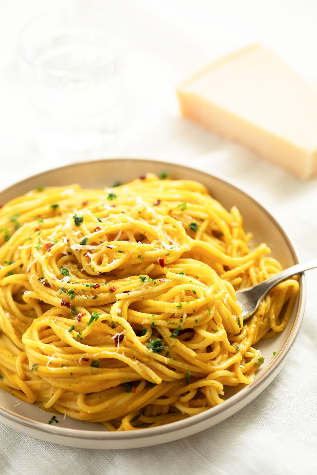plate full of butternut squash sauce pasta and a wedge of parmesan behind it.