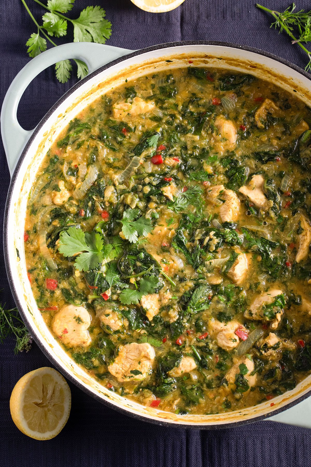 lentil and chicken curry with spinach in a large dutch oven, some lemon halves beside the pot.