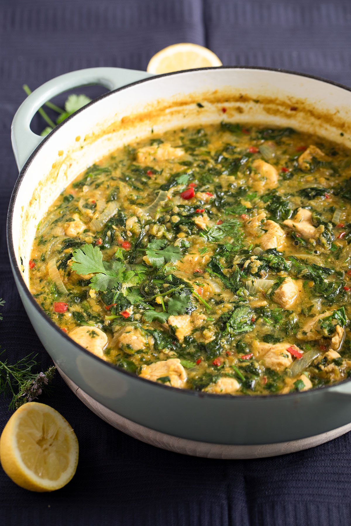a pot full of curry with chicken, lentils, and spinach and half a lemon beside it.