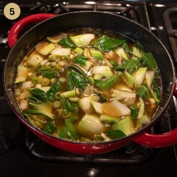 asian soup with noodles, chicken and pak choi simmering in a large pot.