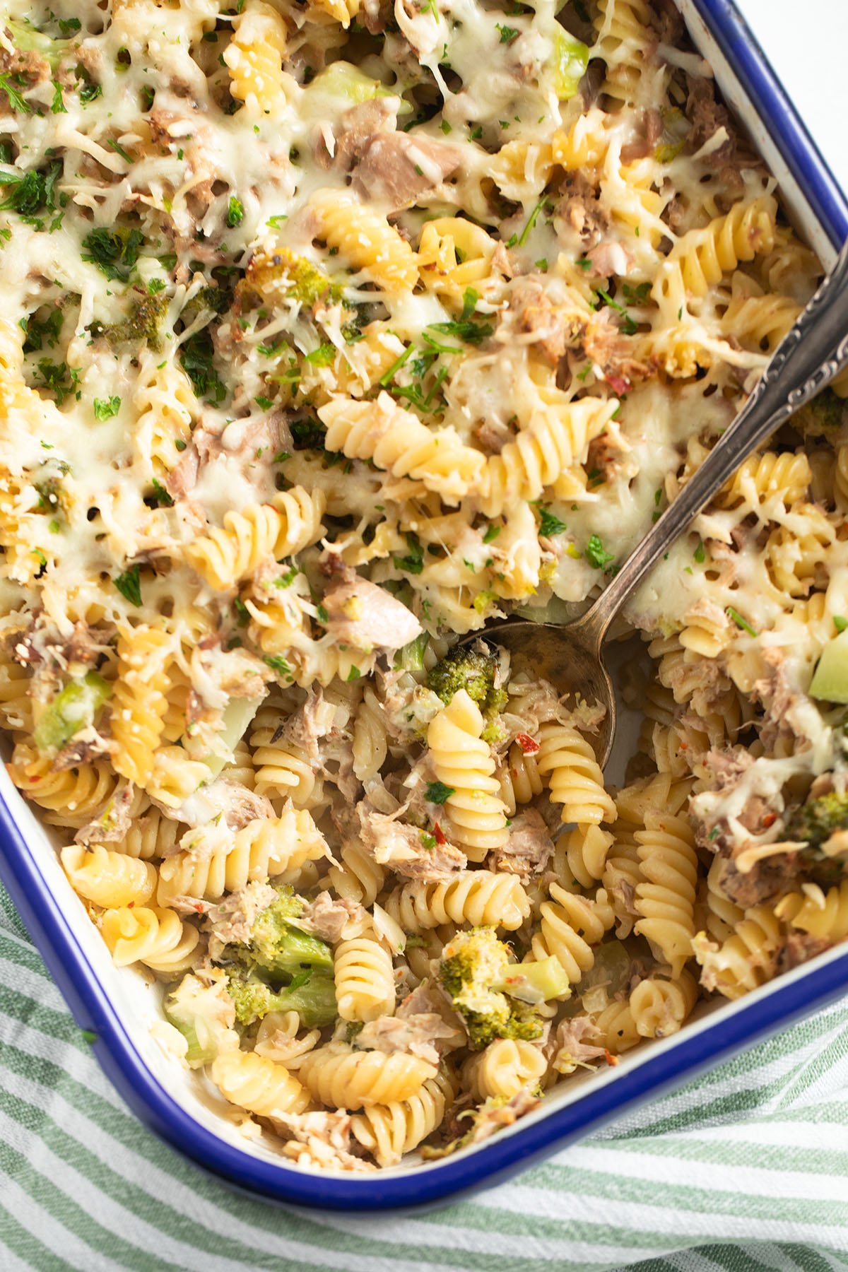 a baking dish full of pasta bake with tuna, broccoli and cheese with a spoon in it.