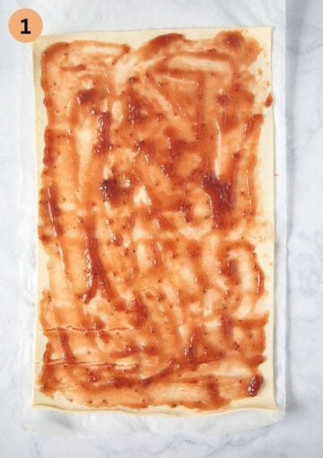 a rectangular sheet of puff pastry with strawberry jam on it.