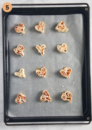 unbaked puff pastry hearts with jam on a lined baking sheet.