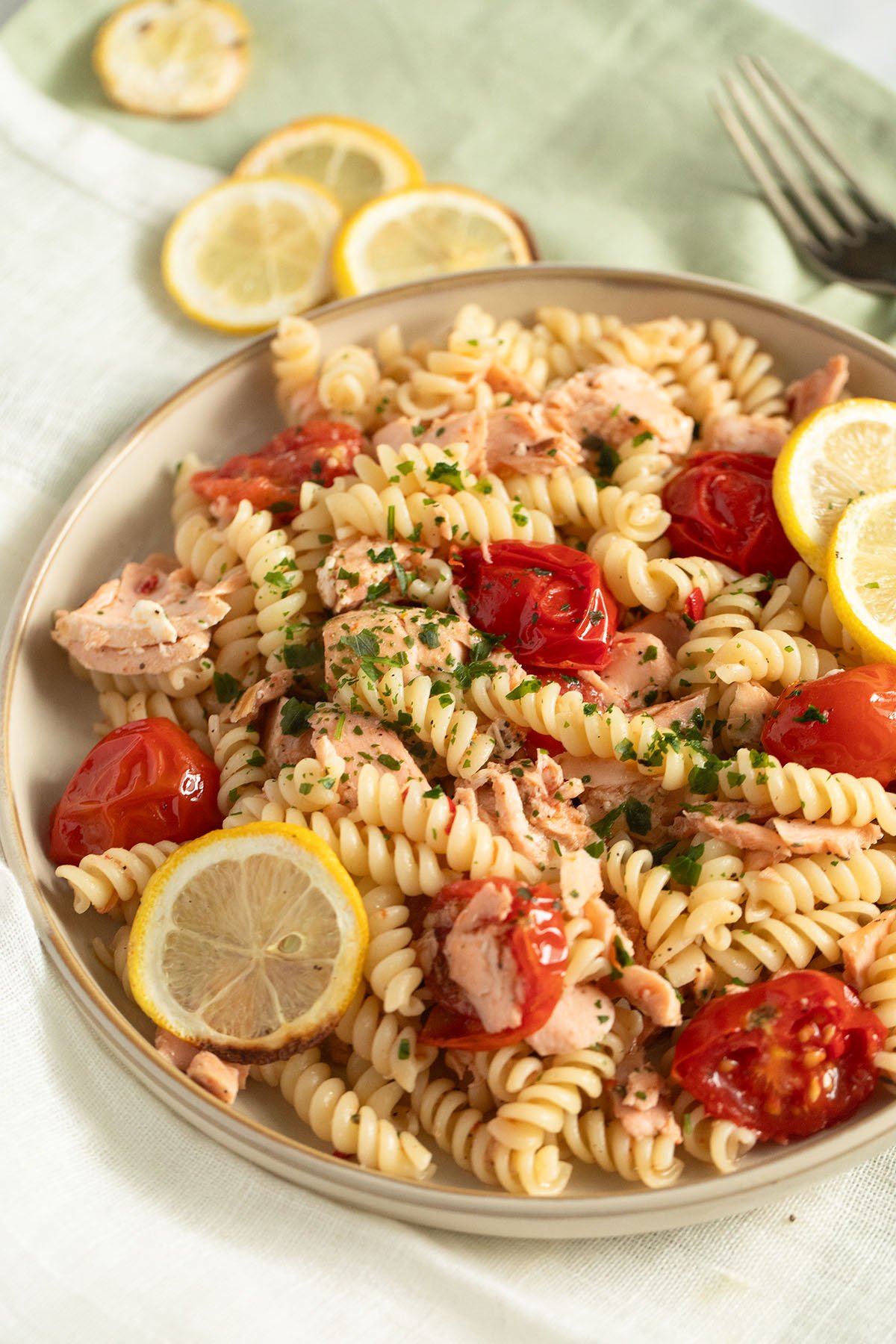 a bowl full of no cream pasta with salmon, tomatoes, and lemon slices; more lemon slices in the back.