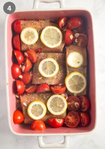 four salmon fillets, halved small tomatoes and lemon slices in a baking dish before cooking.