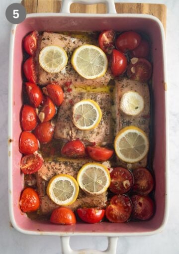 baked salmon with tomatoes, garlic and lemon slices in a baking dish.