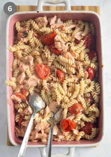 mixing cooked fusili pasta with flaked salmon, halved tomatoes and olive oil in a baking dish.