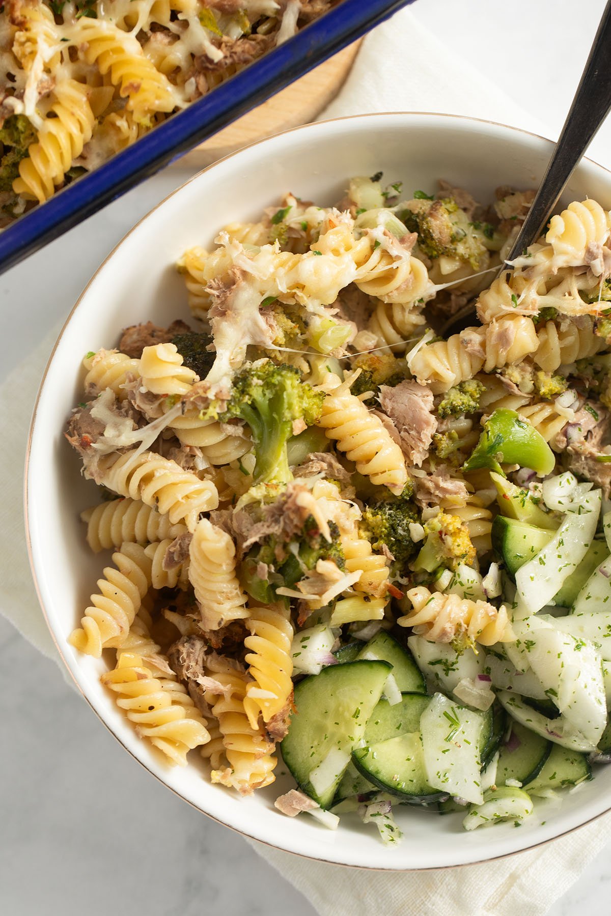 broccoli and tuna pasta served with cucumber salad in a bowl with a spoon in it.