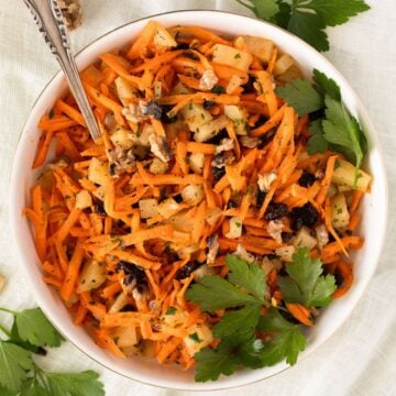 carrot pineapple salad with large parsley leaves on top in a bowl.