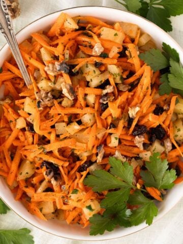 carrot pineapple salad with large parsley leaves on top in a bowl.