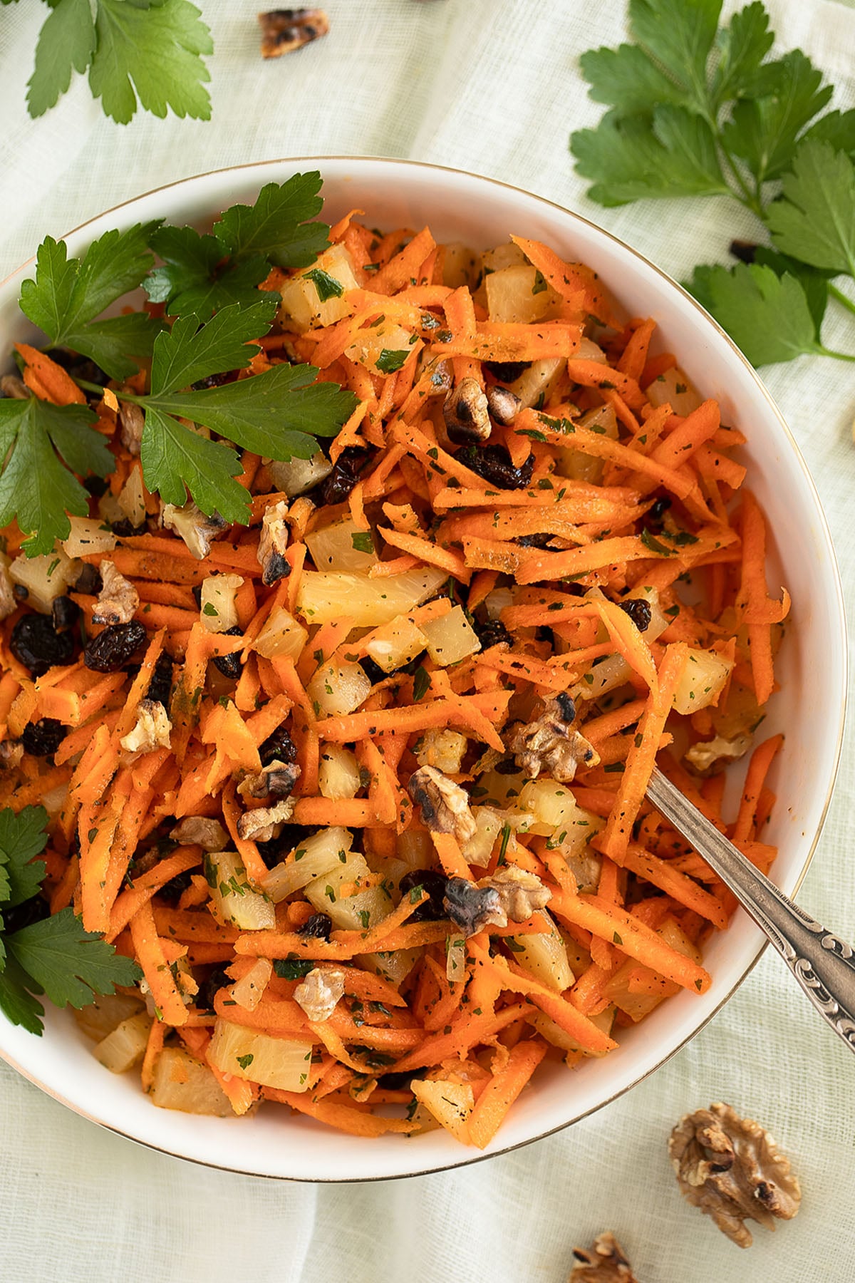pineapple and carrot salad with raisins and walnuts in a large bowl with a spoon in it.