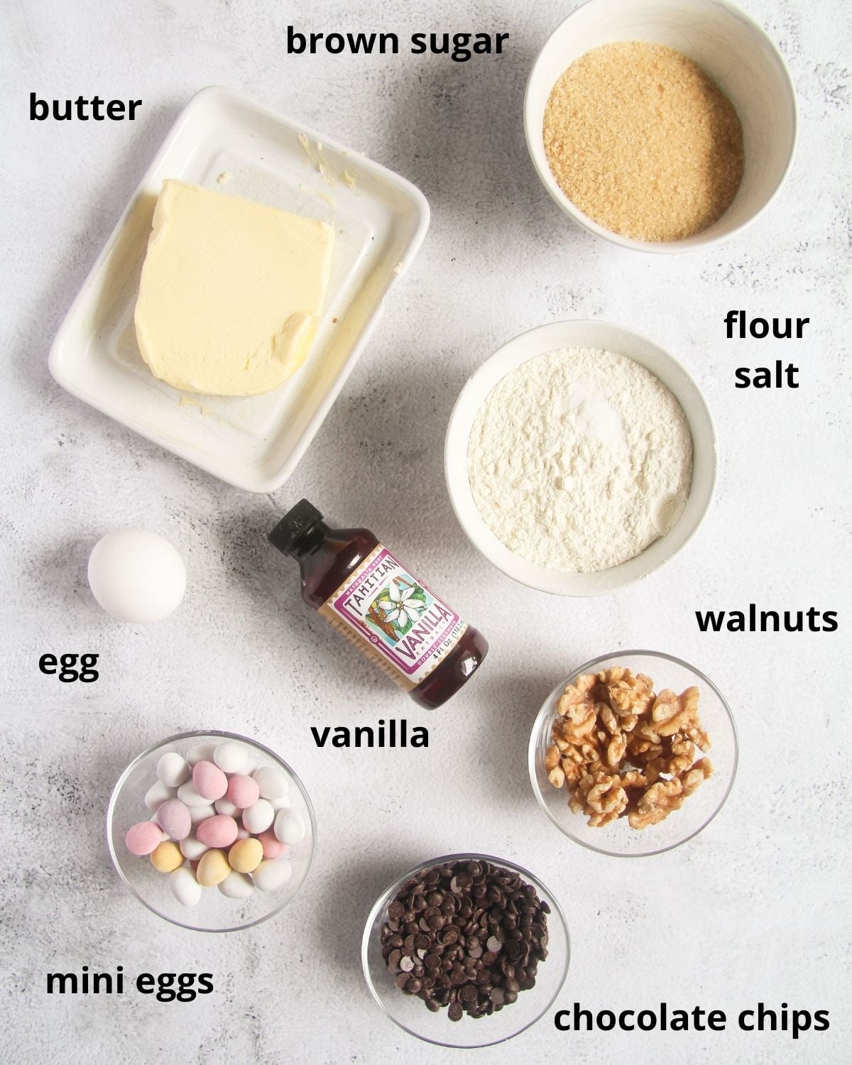labeled ingredients for making cookie bars with mini eggs, butter, brown sugar, walnuts, and chocolate chips.