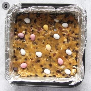 unbaked cookie bars with cadbury mini eggs in lined cookie tin.