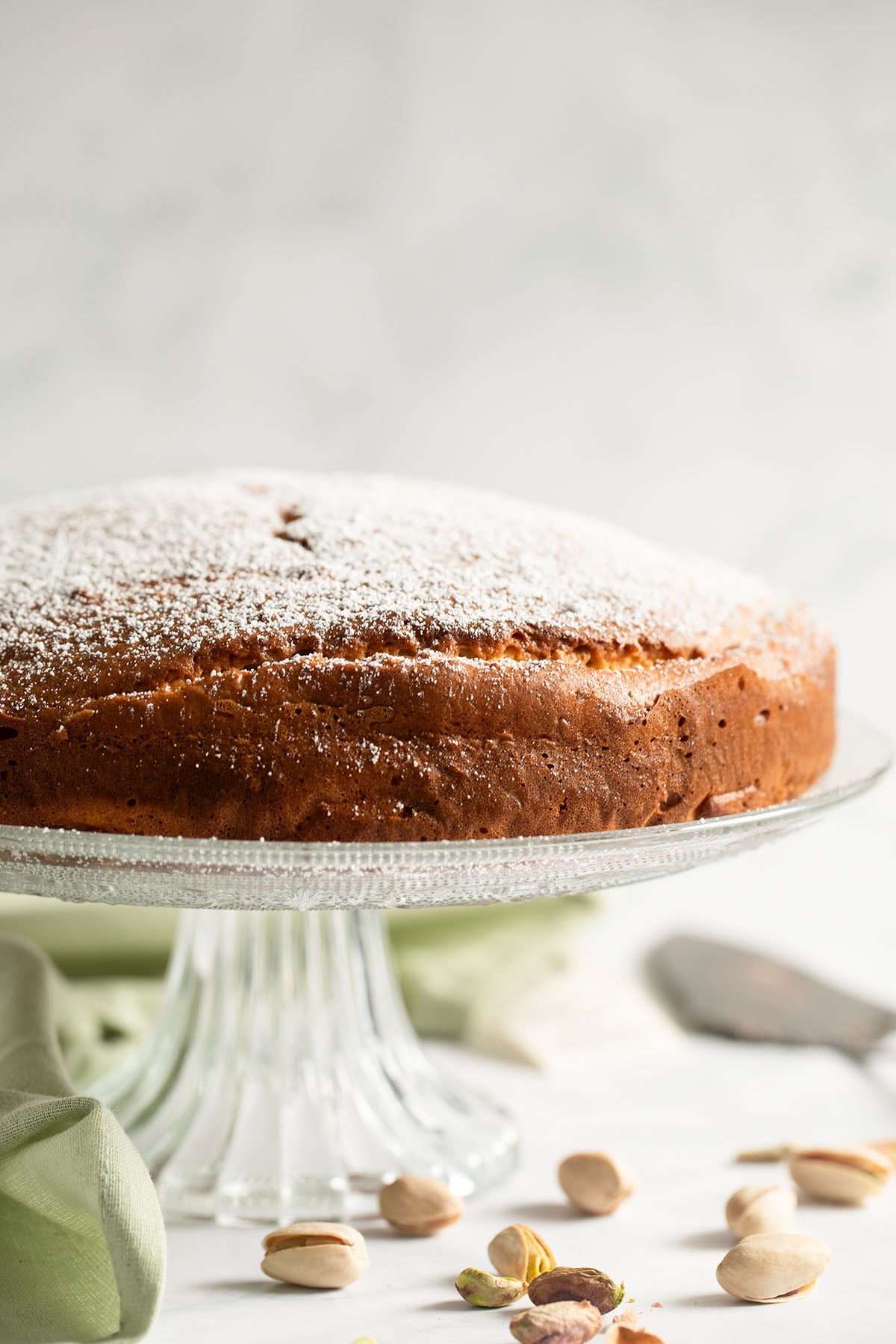 ricotta and pistachio cake sprinkled with confectioners sugar on a cake platter.