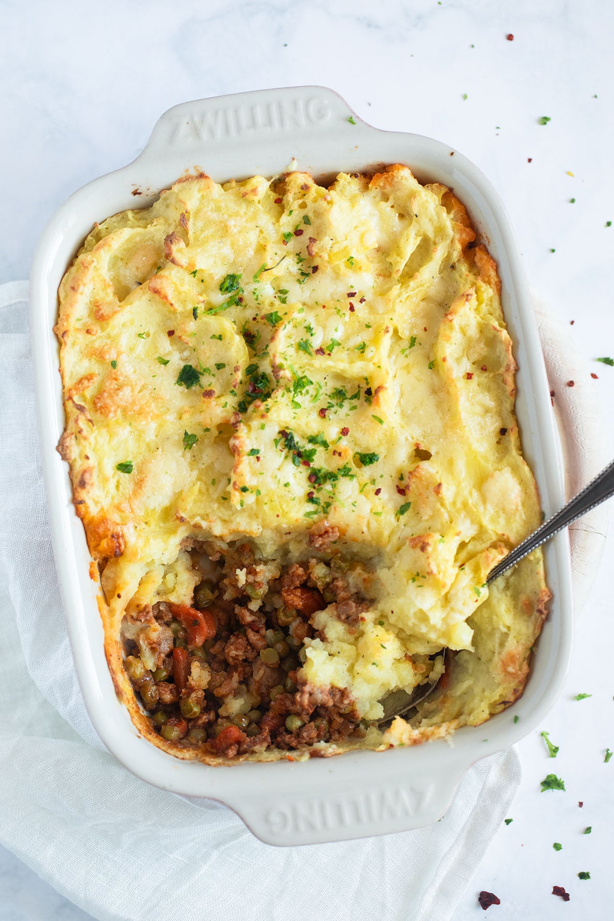 pork sausage shepherd's pie in a bakign dish with a spoon in it and showing some of the meat filling.