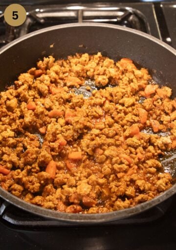 cooking ground pork sausage meat with carrots in a pan.