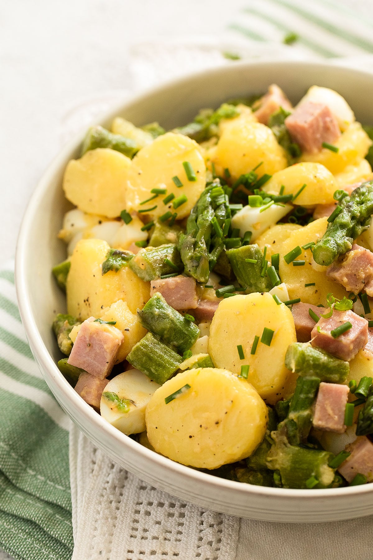 asparagus and potato salad with chives, eggs, and ham in a bowl.