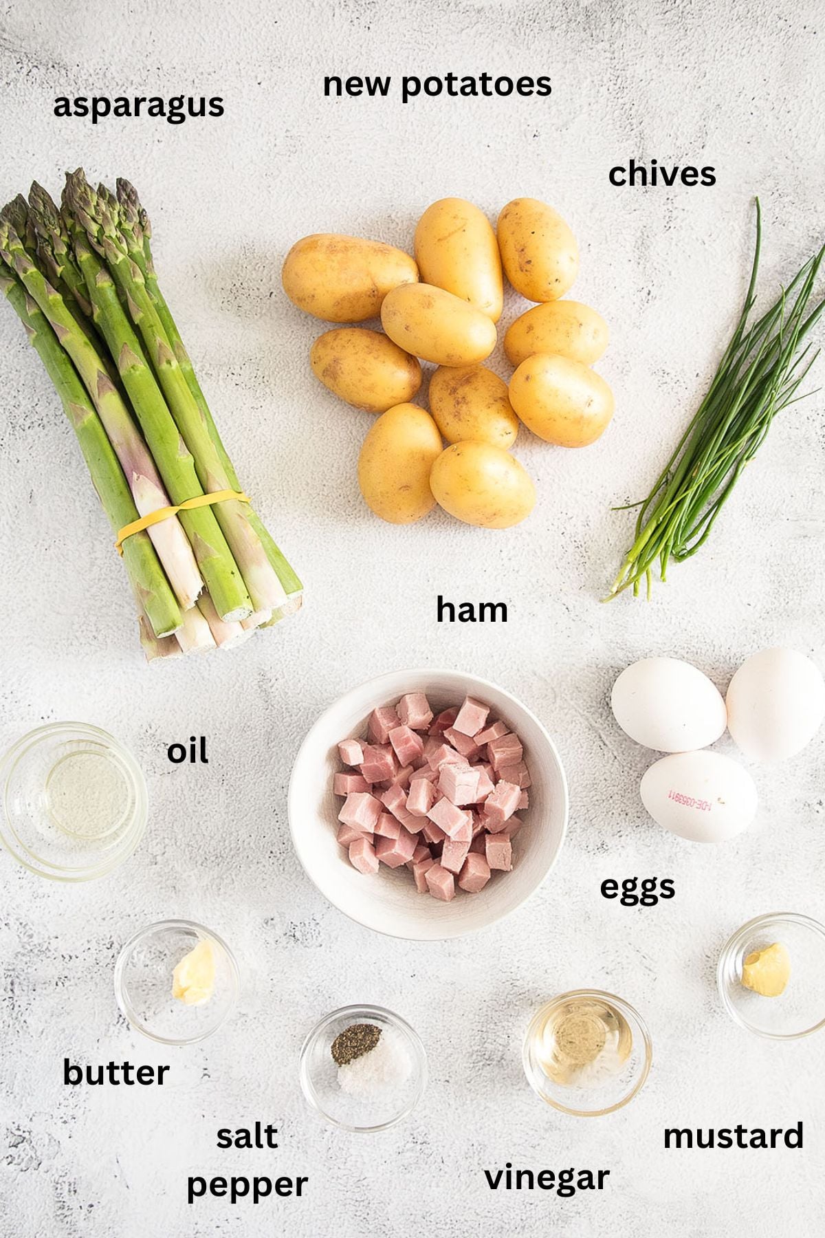 labeled ingredients for making potato salad with asparagus, eggs, ham, chives and oil and vinegar dressing.