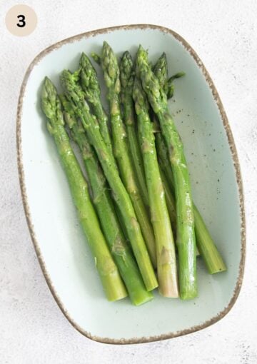 cooked asparagus spears marinating on a long platter.