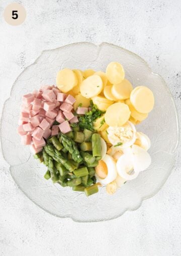 ingredients for making potato salad with asparagus, ham and hard boiled eggs in a bowl.