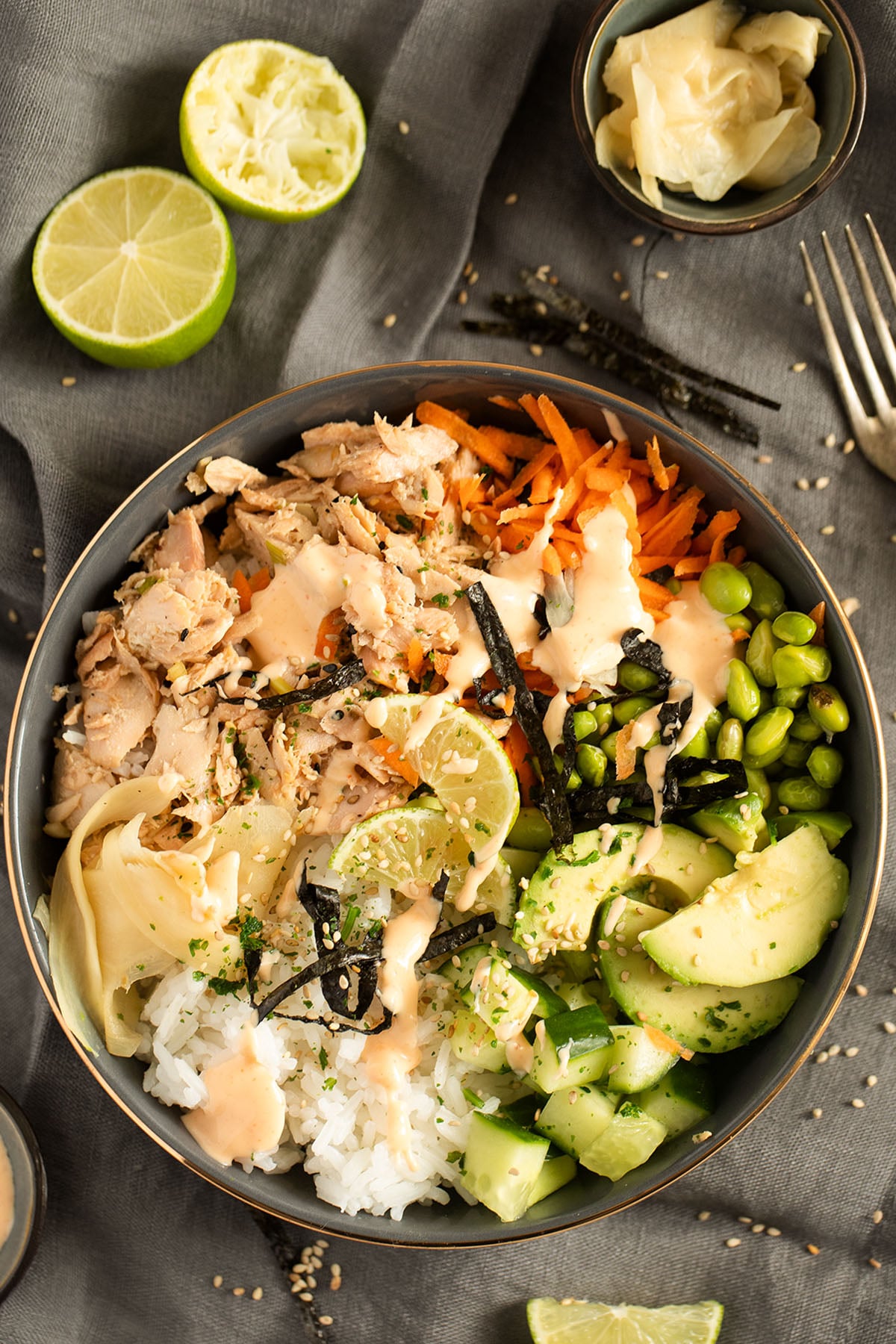 poke bowl with baked salmon, avocado, rice and vegetables, lime and pickled ginger beside it.