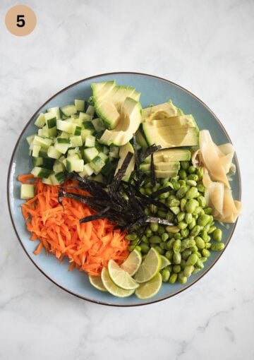 chopped avocado, cucumber, grated carrots, lime slices, nori sheets, edamame and pickled ginger on a plate.