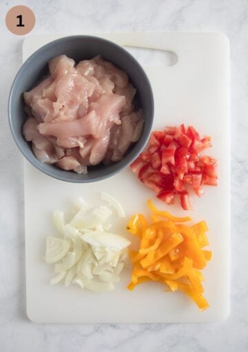 a bowl of sliced chicken, sliced peppers, onions and tomatoes.