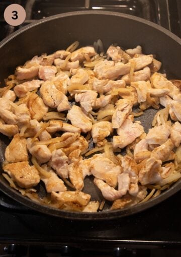 searing chicken and sliced onions in a pan.