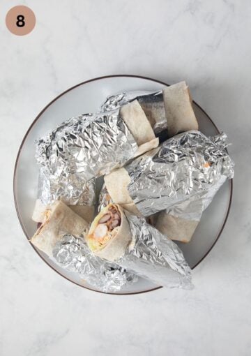 halved chicken wraps wrapped in foil on a large plate.