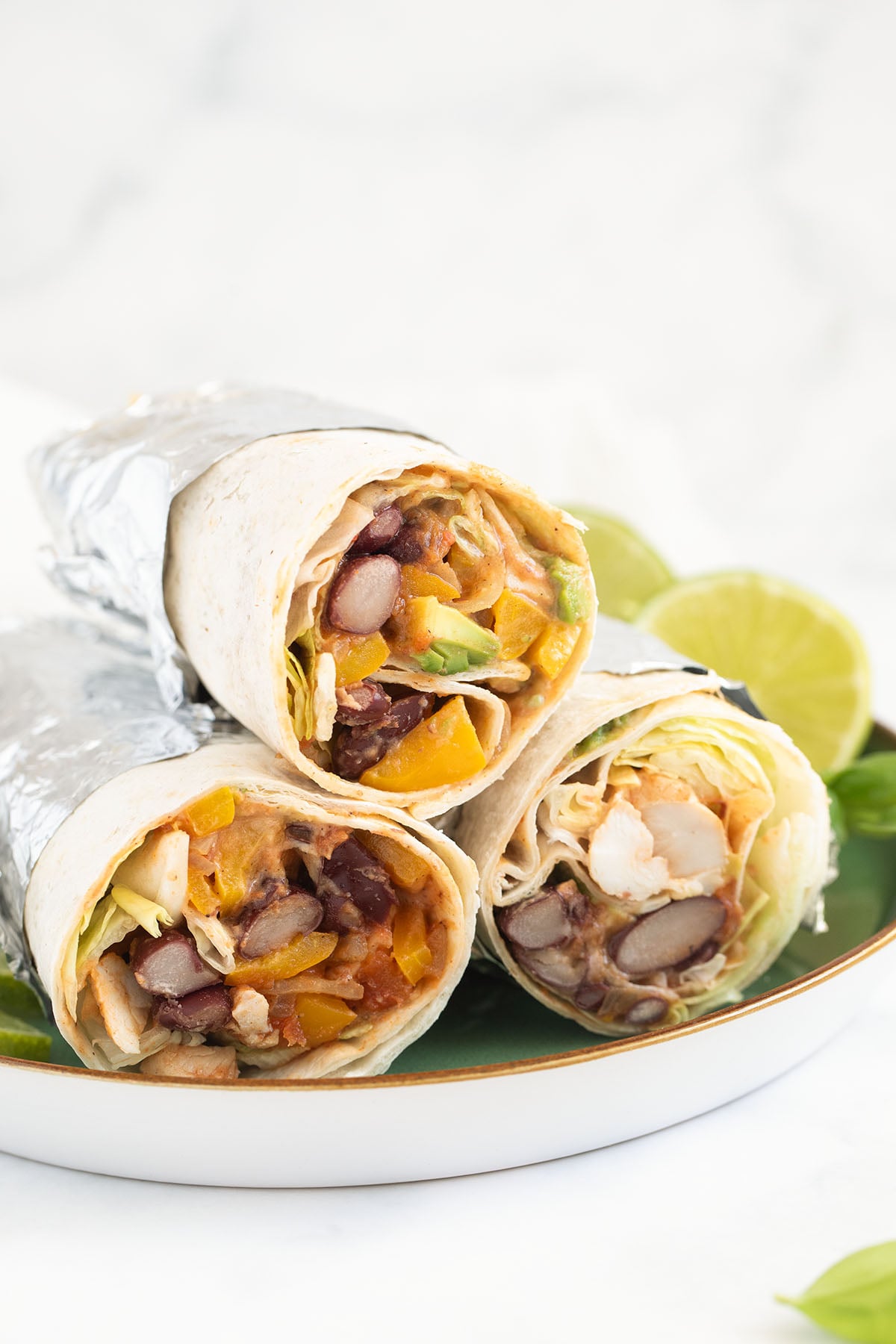 three mexican chicken wraps and lime wedges on a plate.