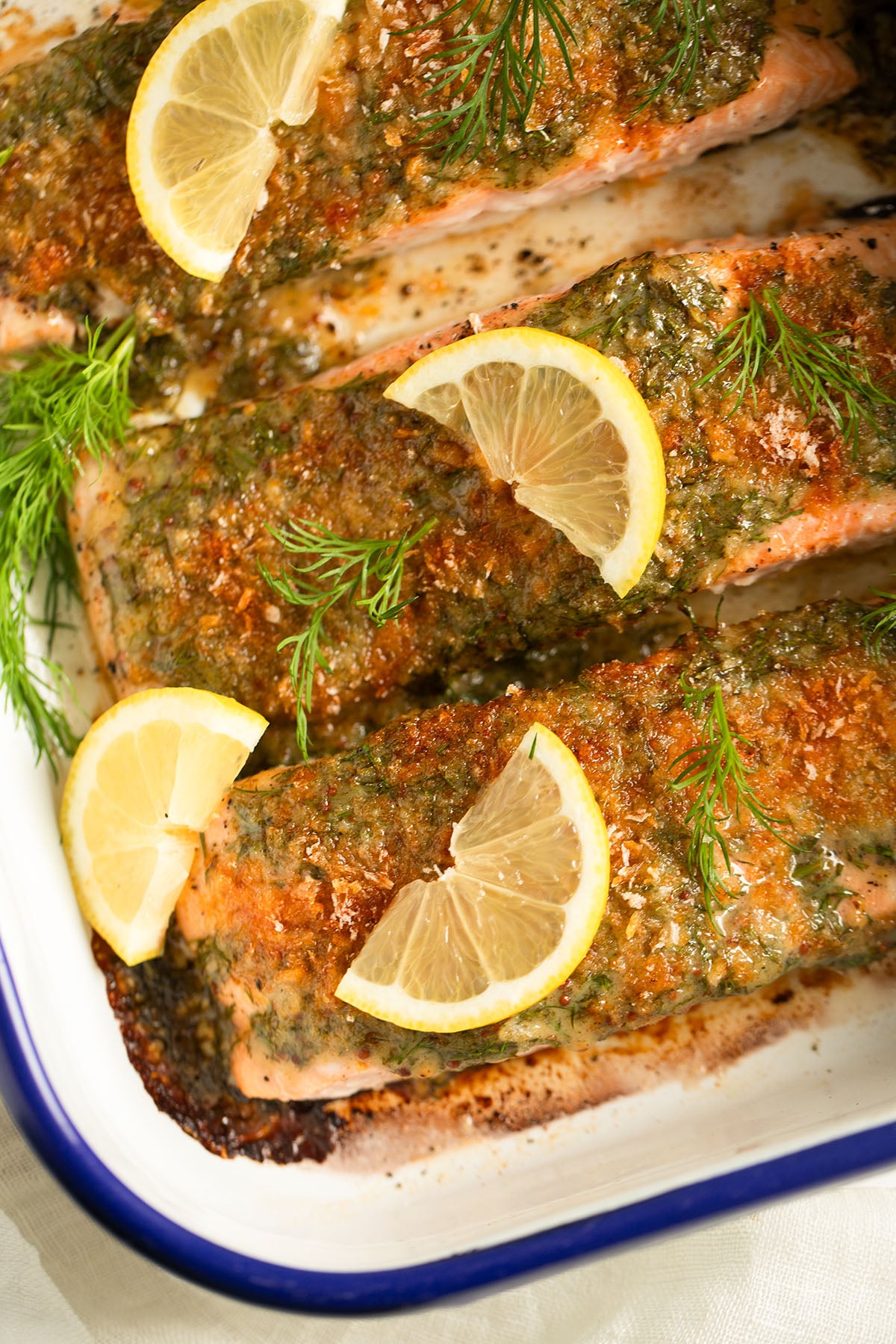golden baked salmon fillets with mustard dill topping and lemon slices on top.
