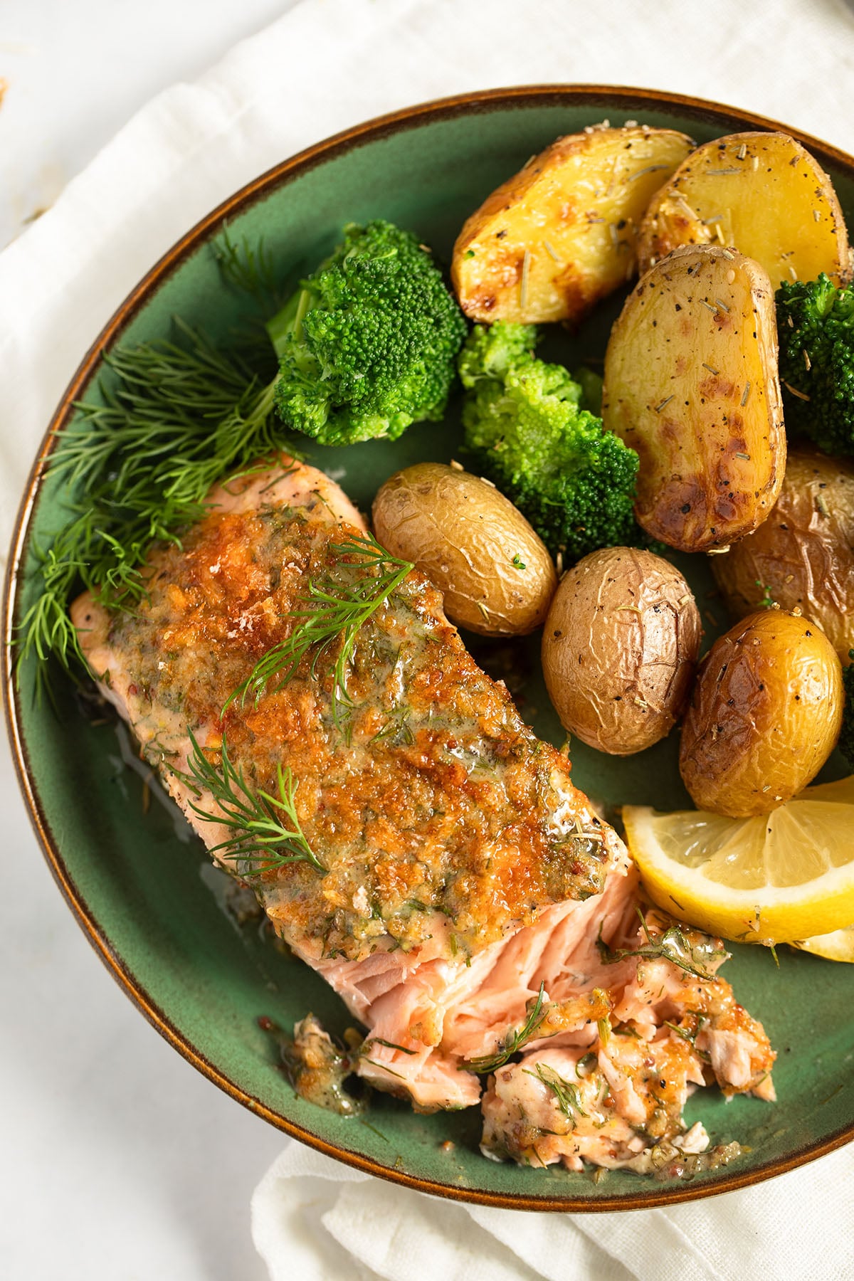 salmon with dill and mustard served with small potatoes and broccoli on a plate.