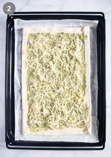 spreading cream cheese and pesto mixture and cheese on a sheet of puff pastry on a baking sheet.