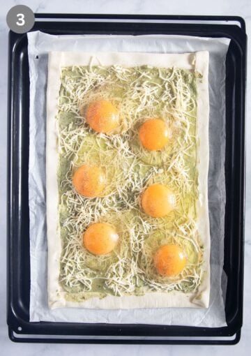 six raw eggs on top of a puff pastry sheet spread with pesto and cheese.