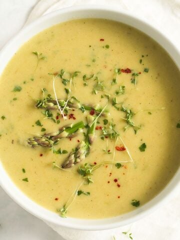 potato and asparagus soup sprinkles with herbs in a large bowl.