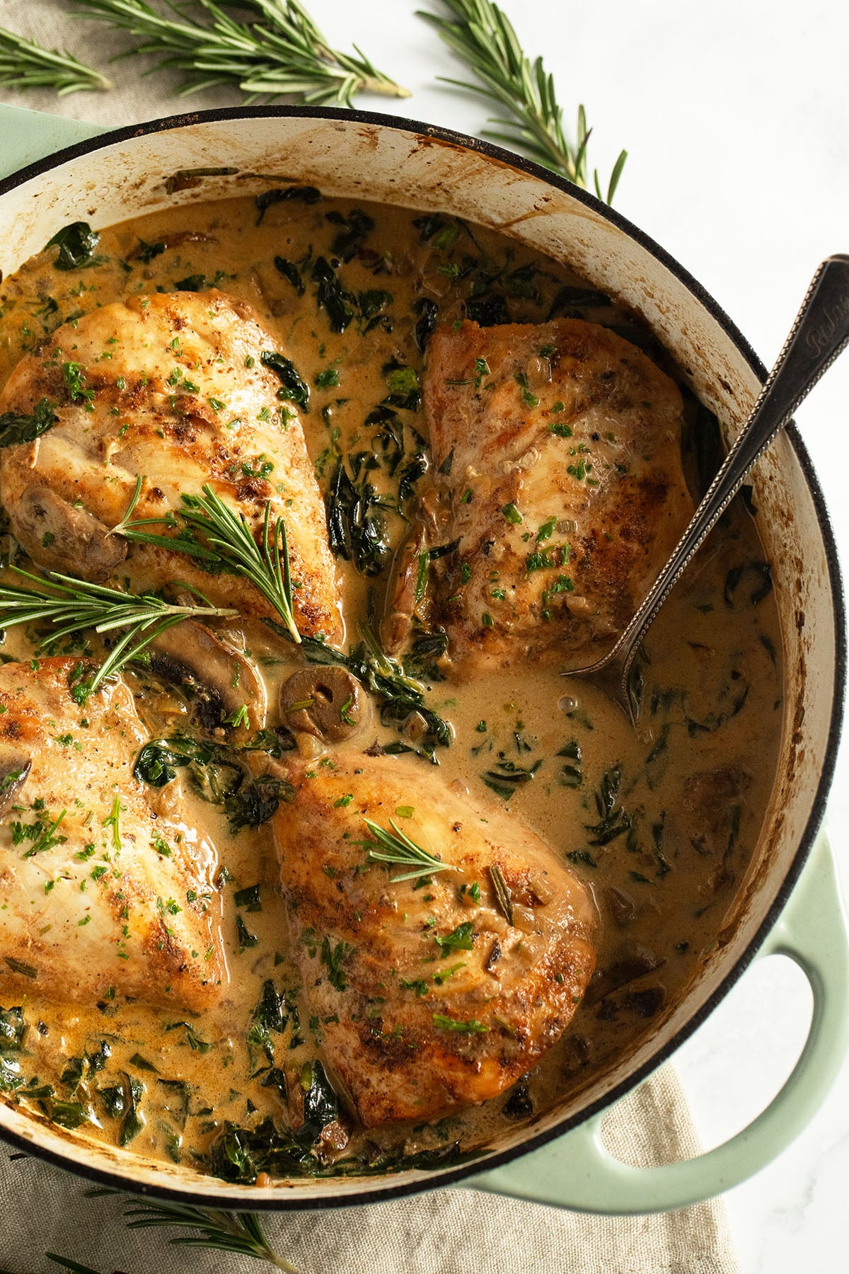 four chicken breasts in mushroom and spinach sauce with cream in a pot.