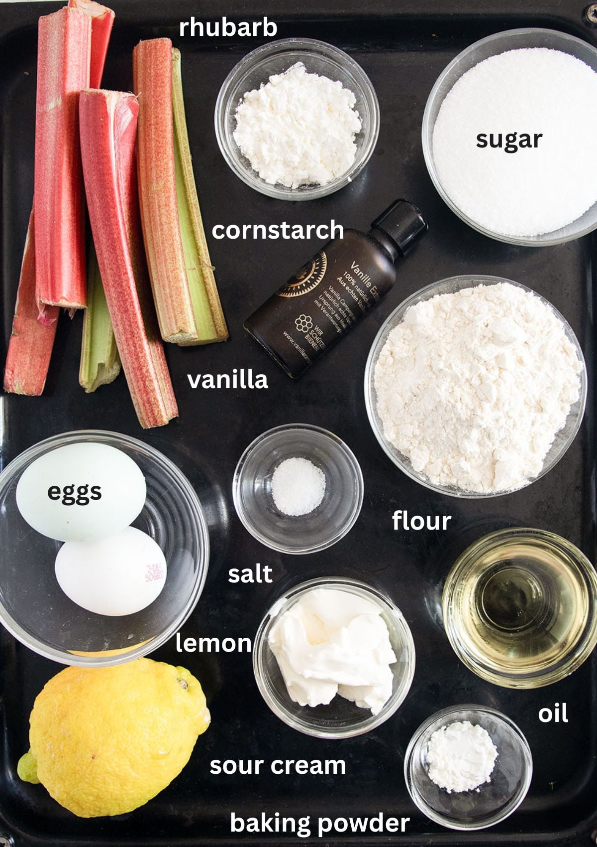 labeled ingredients for making a cake with rhubarb, sour cream, eggs, lemon, flour, oil.