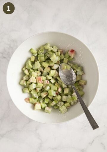 mixing chopped rhubarb with cornstarch and sugar in a bowl with a spoon.