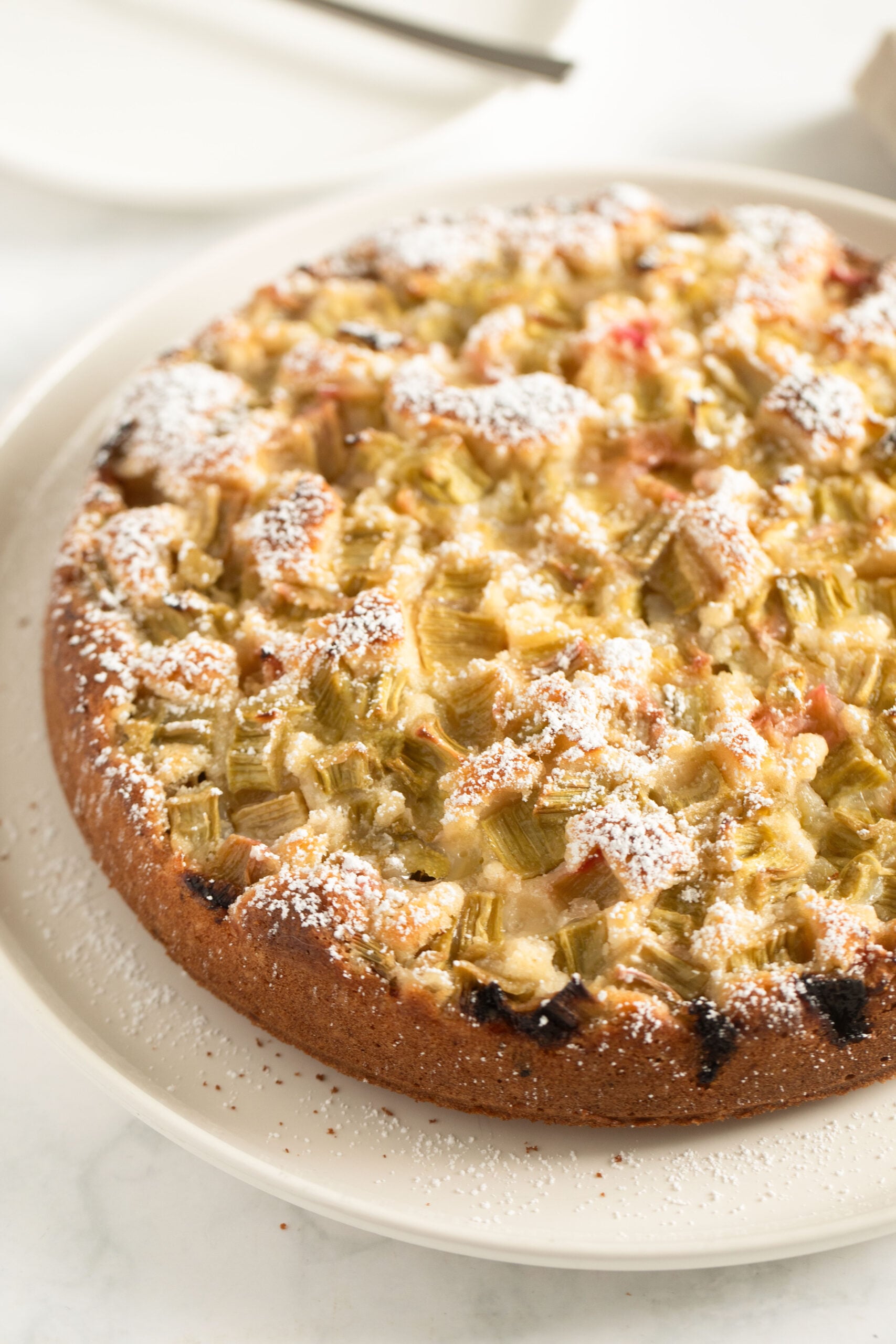 rhubarb and sour cream cake dusted with icing sugar on a cake plate.